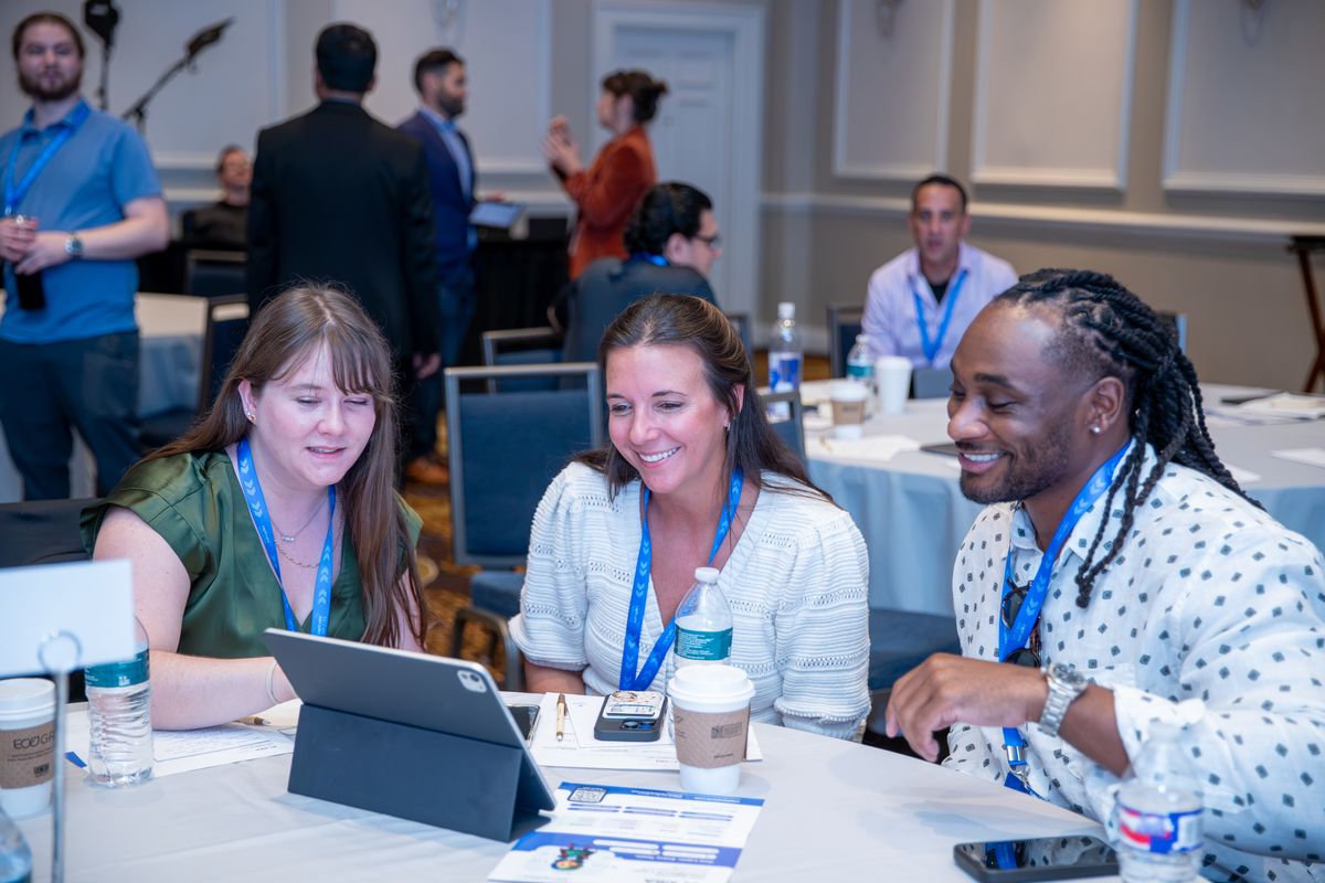 Three attendees laughing at a table with tablets open